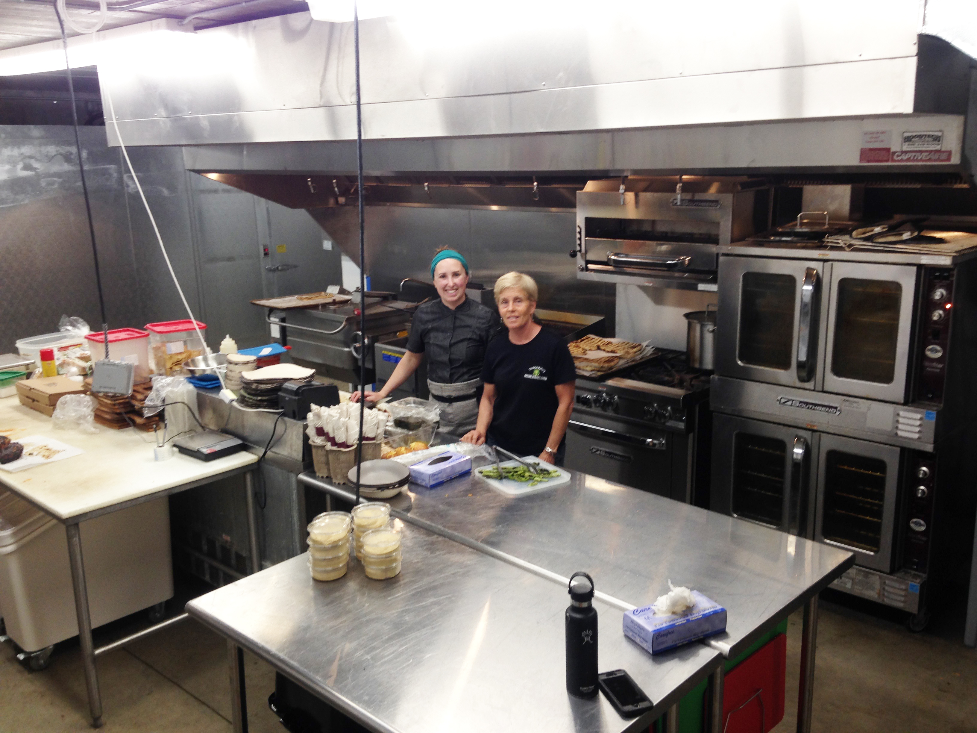 Shown is Laura Tangerini, right, with her head chef, in the newly-built kitchen underneath The Farmer’s Porch at Tangerini’s Farm, which will offer a lunch menu of locally produced food. Tangerini’s will host a school year-end summer-start bash on June 19th, with a concert by the Phat Daddies at 6 p.m.